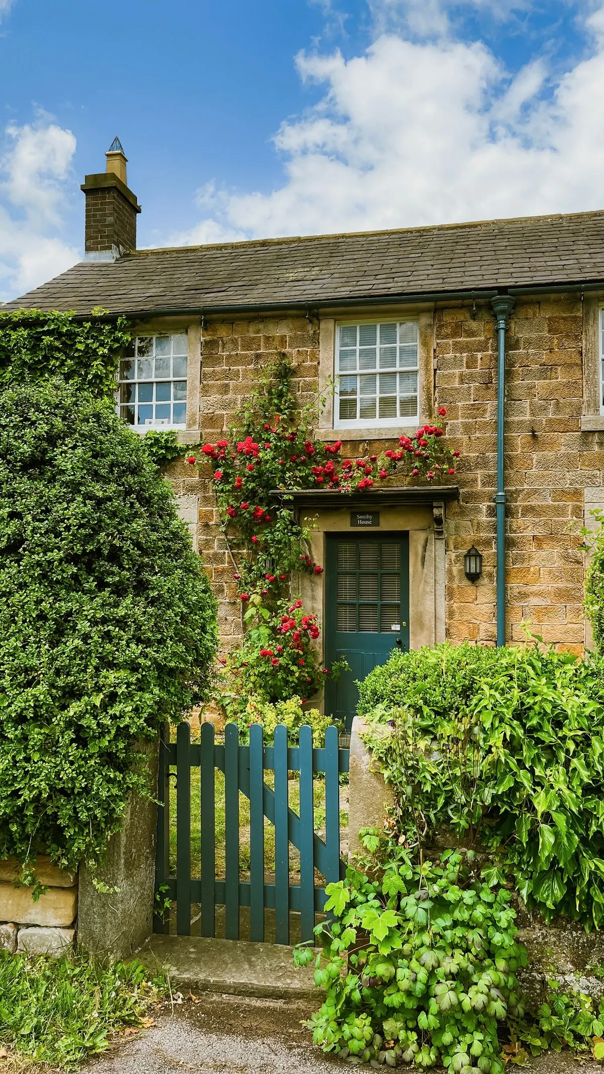 Stone cottage with a green front door, climbing roses and a garden shrub