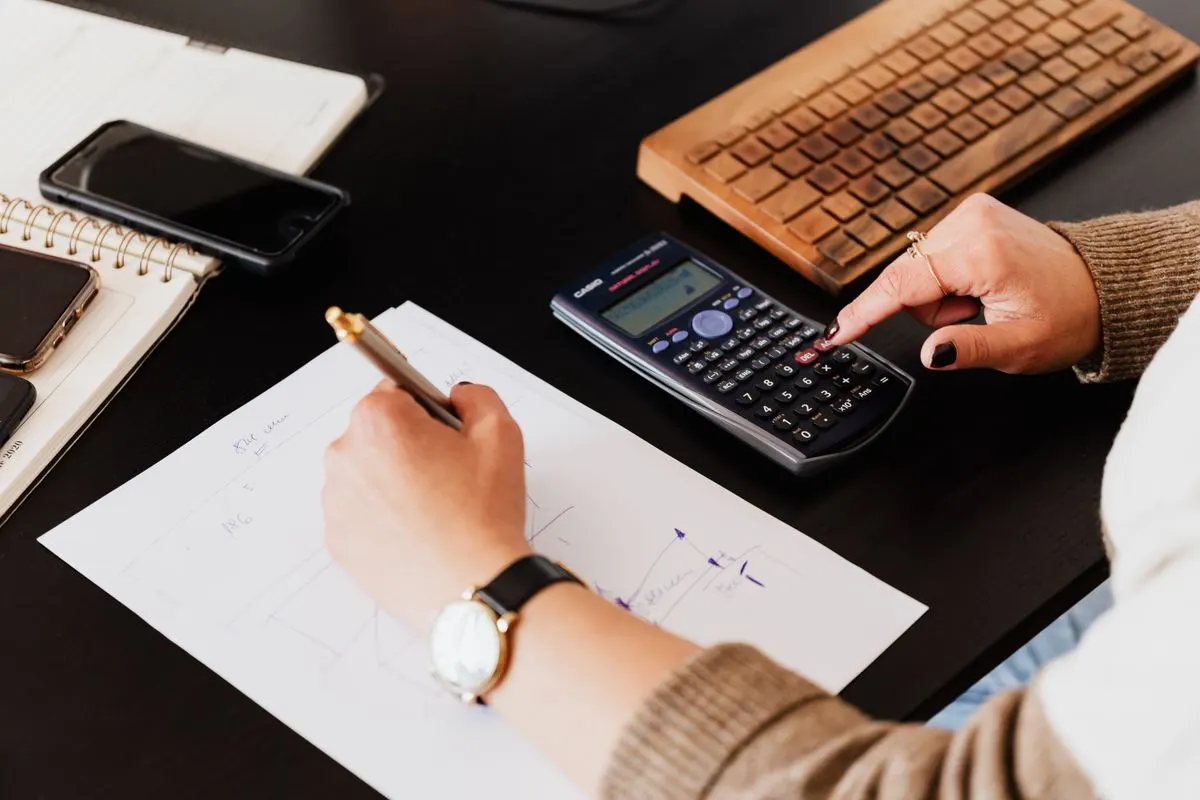 Hands writing in a notebook while using a calculator at a desk