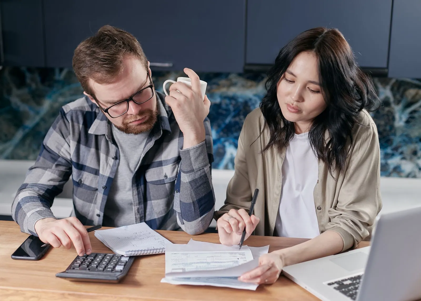 Couple reviewing household bills at a kitchen table with a calculator and laptop