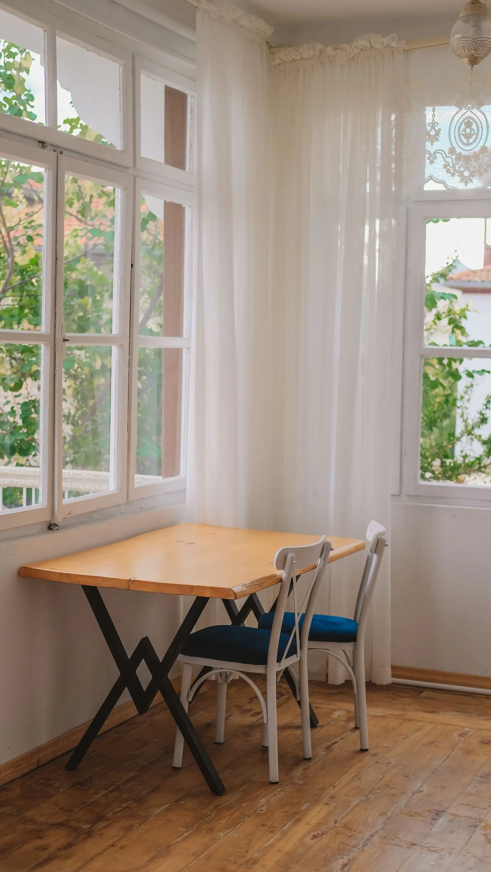 Corner of a home interior with a wooden table, chairs and sheer curtains