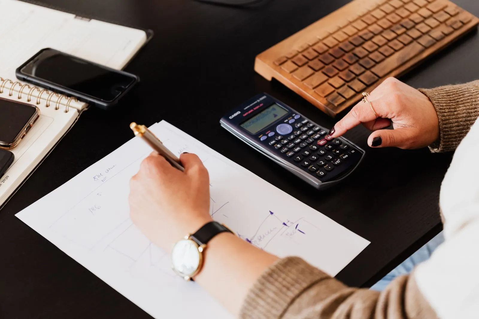 Hands writing in a notebook while using a calculator at a desk