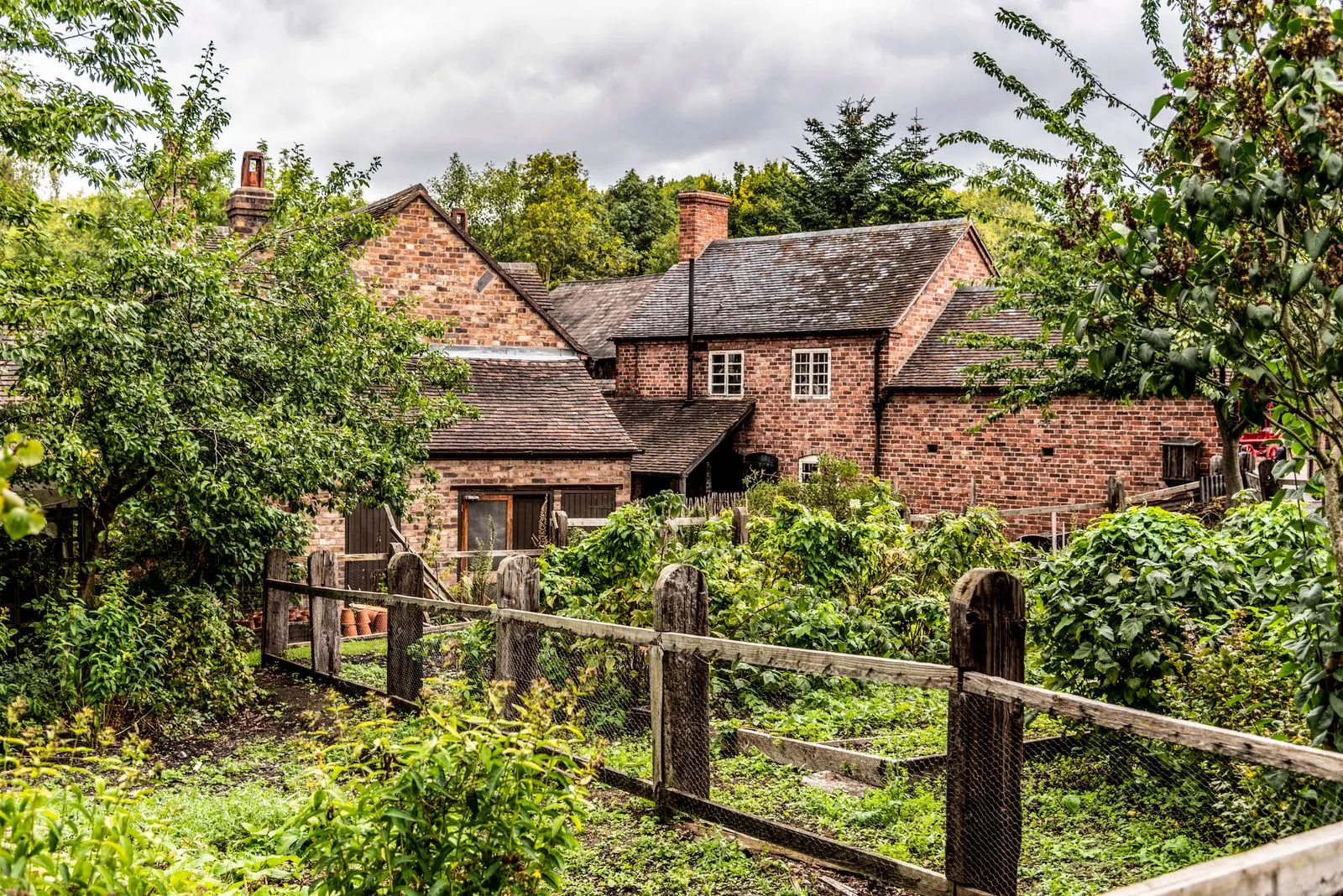 Brick house with a garden and wooden fence among green trees in England