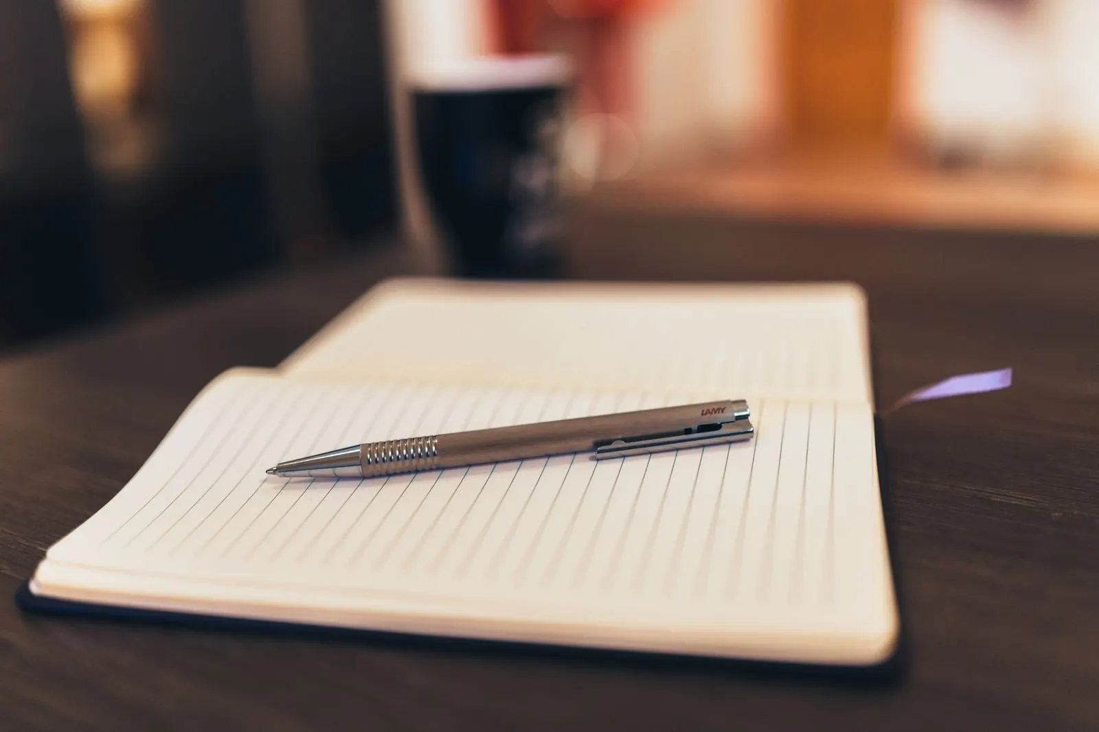 Open notebook and pen on a wooden table, with a mug in the background